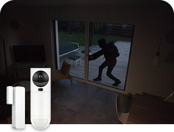 Mustiin pukeutunut henkilö tunkeutumassa asuntoon lasioven kautta pimeässä. Etualalla Verisuren ovi- ja ikkunahälytin sekä GuardVision-videovalvontakamera.