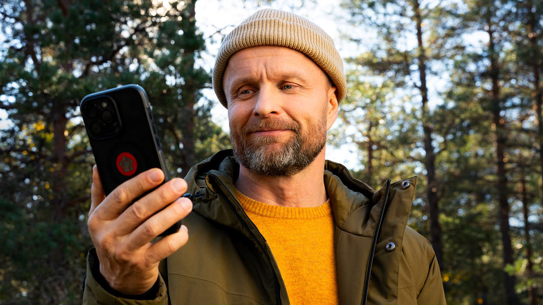 Metsässä oleva mies katsoo kännykkää, jossa on Verisuren sovellus.