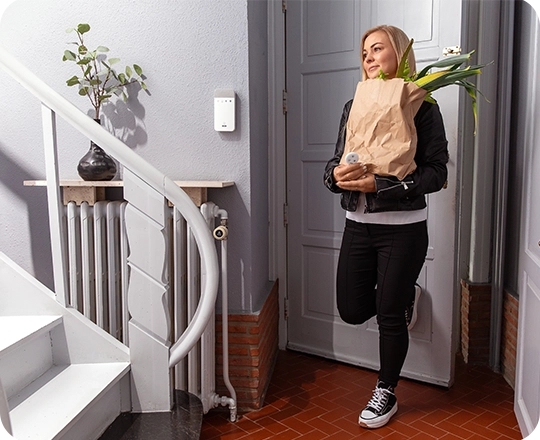 Nainen kävelee sisään ostoskassin kanssa ja pitää Verisuren kauko-ohjainta kädessään.