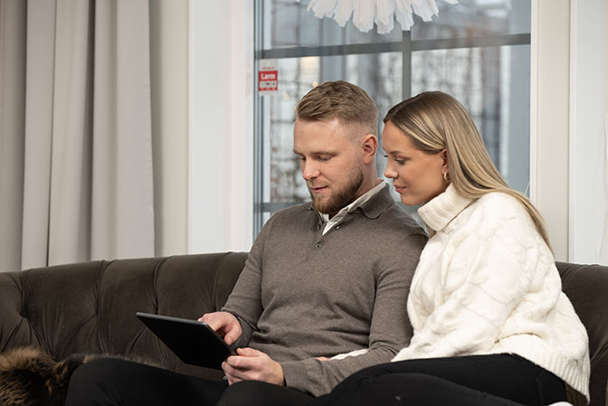 Mies ja nainen sohvalla tutkimassa tabletilta vaihtoehtoja hälytysjärjestelmäksi.
