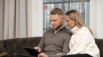 Mies ja nainen sohvalla tutkimassa tabletilta vaihtoehtoja hälytysjärjestelmäksi.