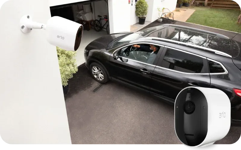 Auto ajaa autotalliin ja kuvan etualalla Arlo-valvontakamera.