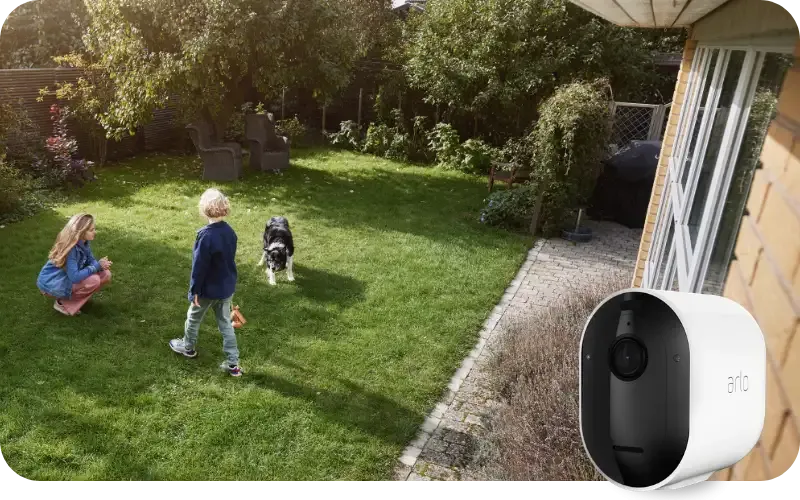 Takapiha, jossa kaksi lasta ja koira. Kuvan etualalla Arlo-valvontakamera.